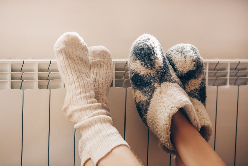 Two Pairs Of Feet With Fuzzy Socks Raised Up On Furnace