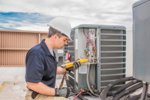 Trained hvac system technician holding a voltage meter, performing preventative maintenance on a air conditioning condenser unit